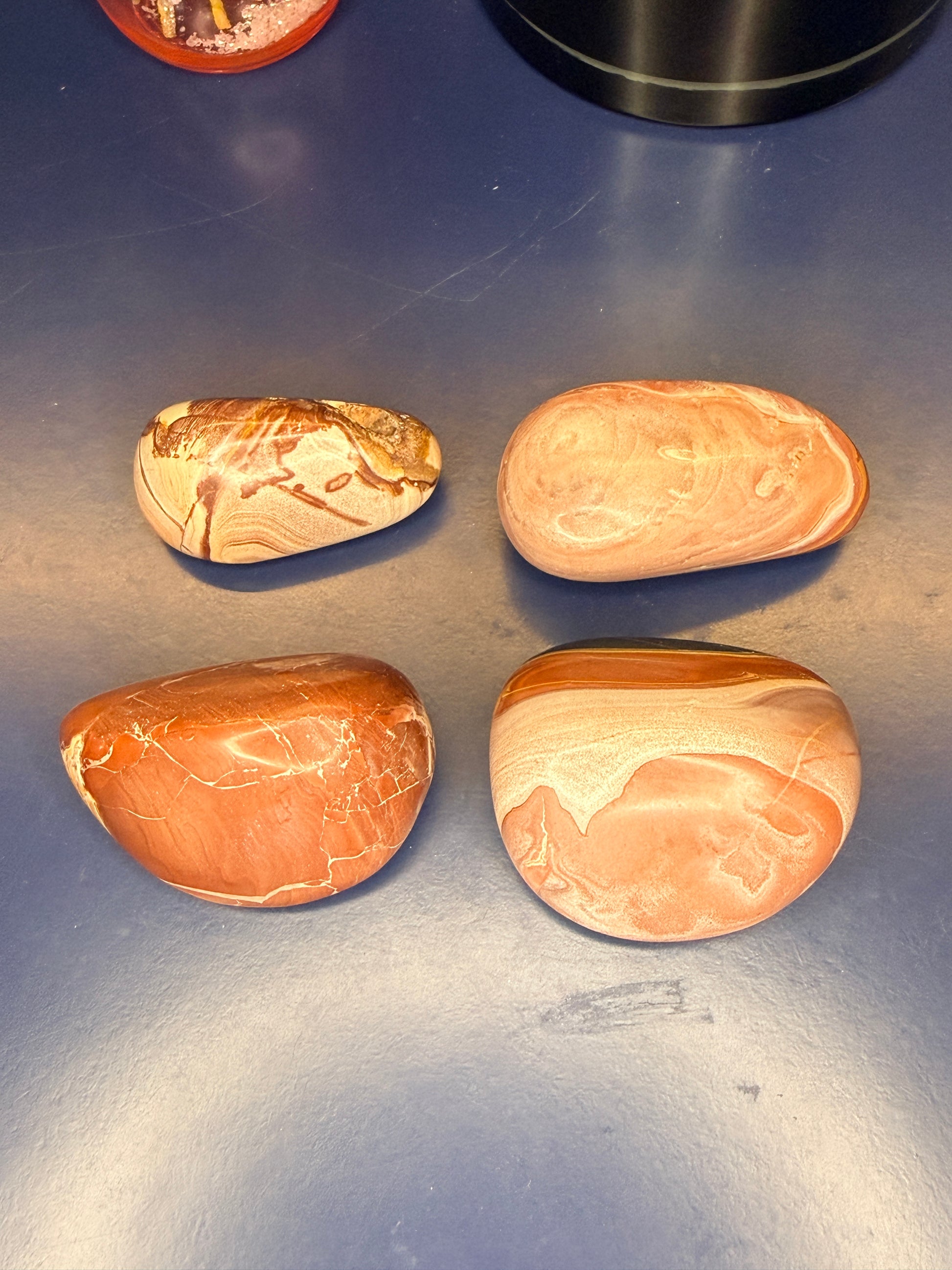 Four marbled red and brown rainbow rhyolite palmstones on a blue background