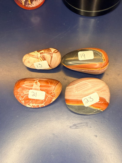 Four marbled red and brown rainbow rhyolite palmstones on a blue background