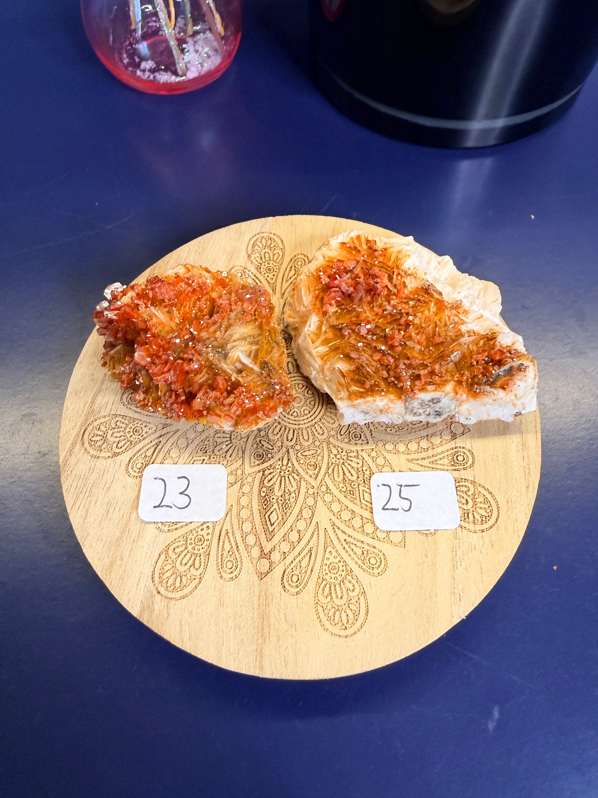 Two bright orange raw crystal clusters on a decorative wooden coaster on a blue background
