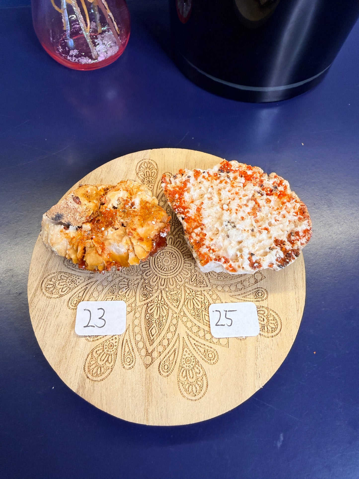 Two bright orange and white raw crystal clusters on a decorative wooden coaster on a blue background