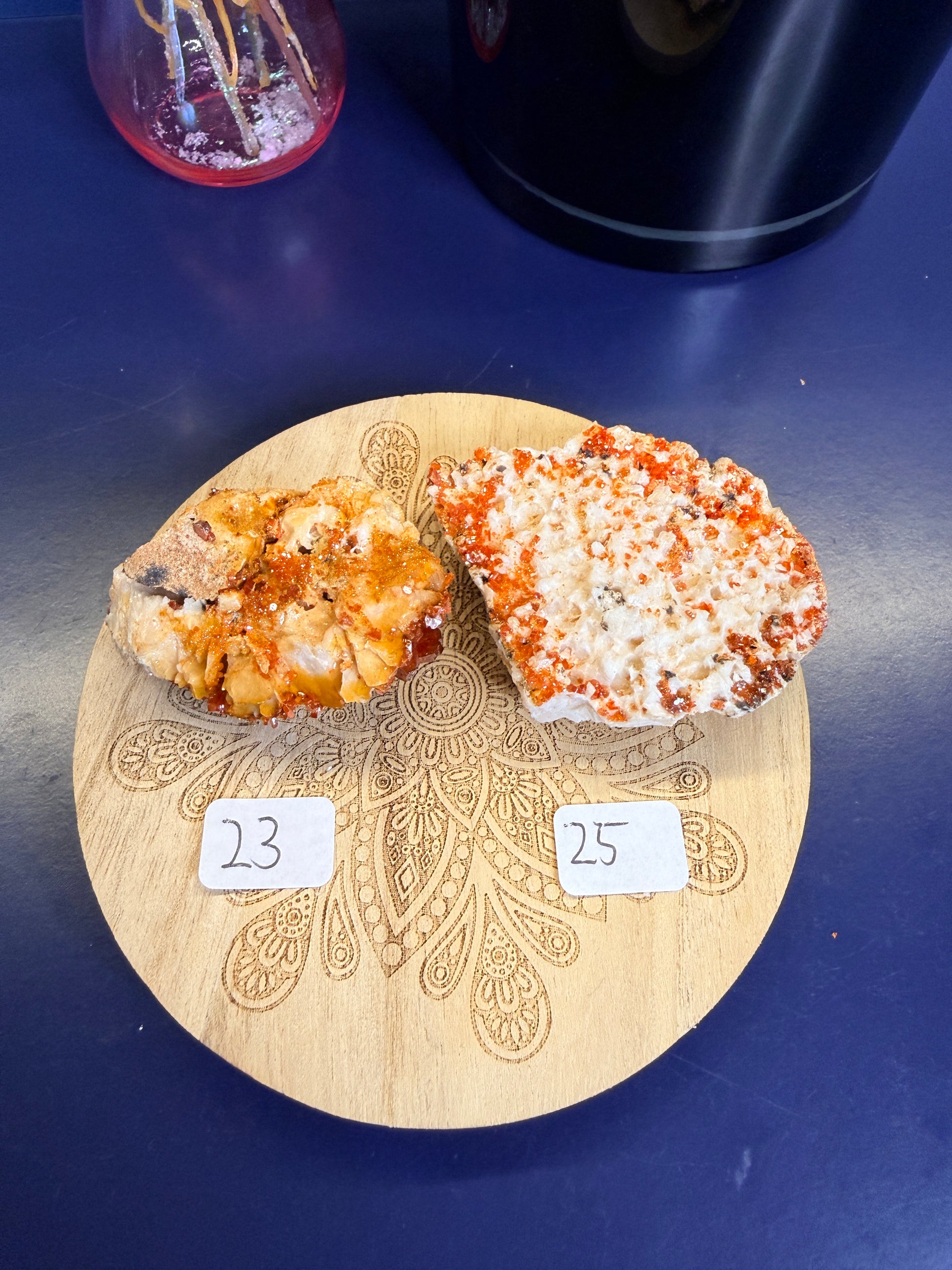 Two bright orange and white raw crystal clusters on a decorative wooden coaster on a blue background