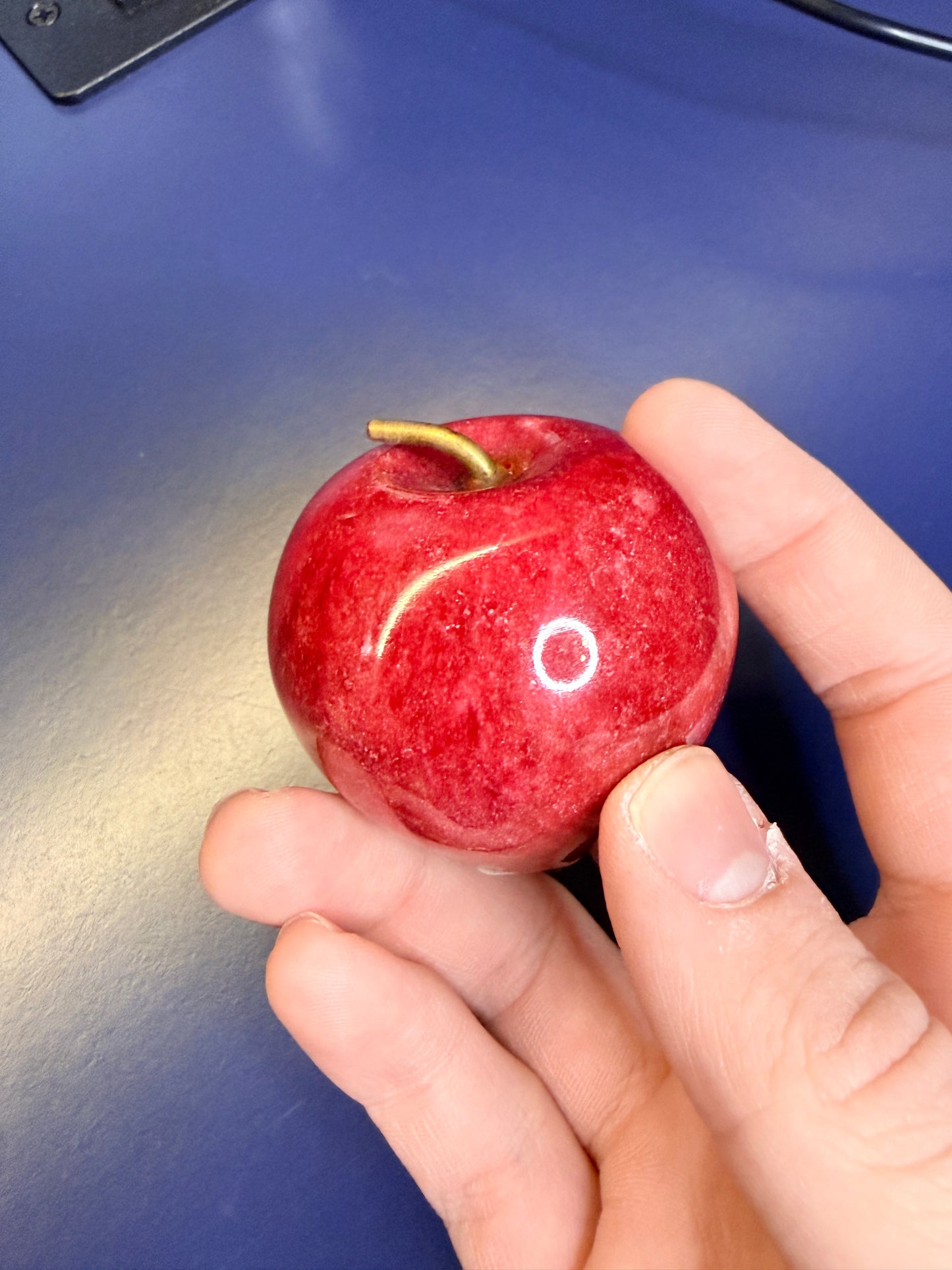 Hand holding a red jasper apple against a blue background