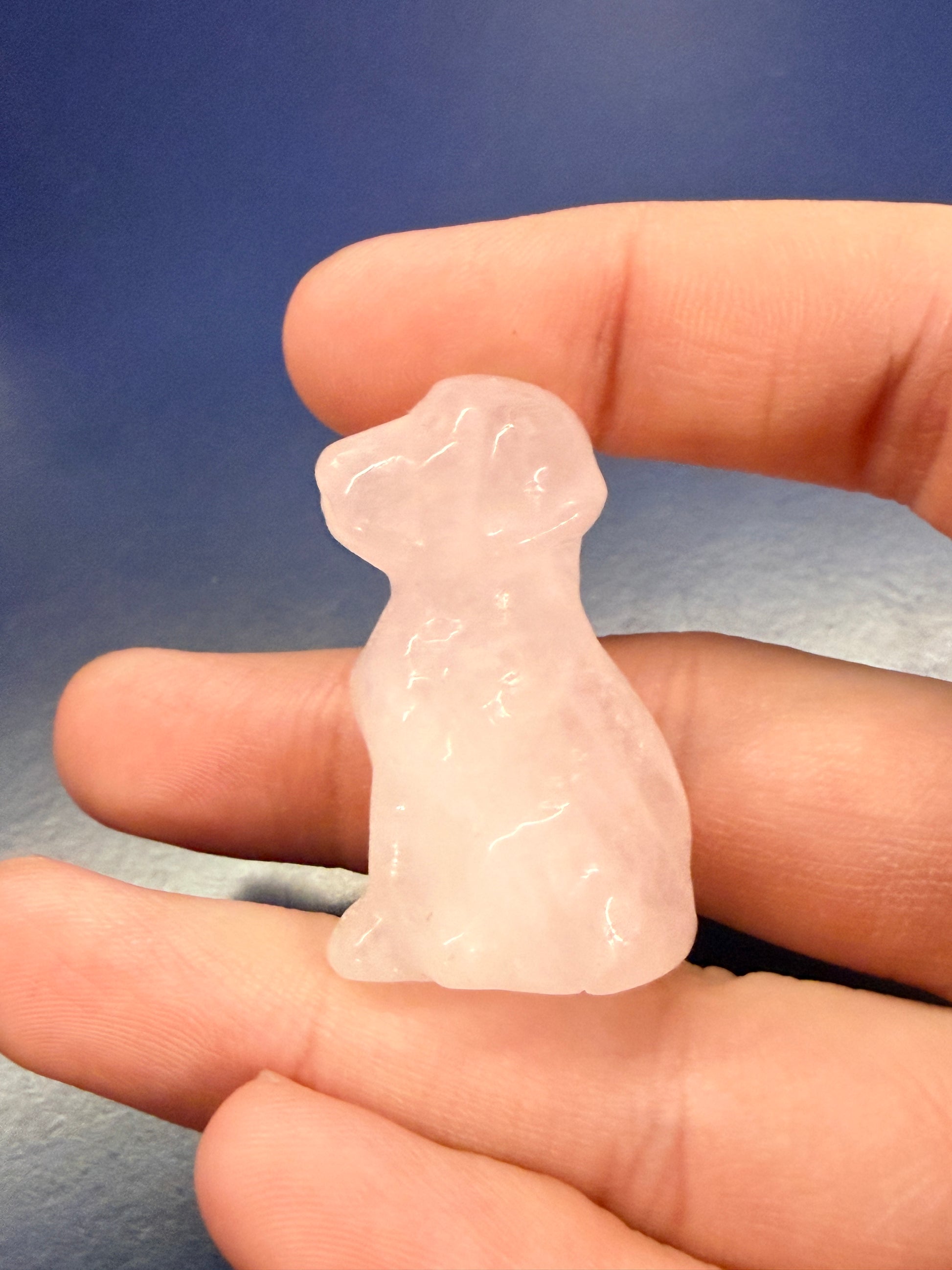Hand holding a rose quartz Labrador dog crystal against a blue background