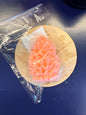 Orange flower-shaped soap on a decorative wooden coaster with clear plastic wrap.
