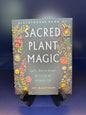 Book titled 'Sacred Plant Magic' with decorative cover on a reflective surface