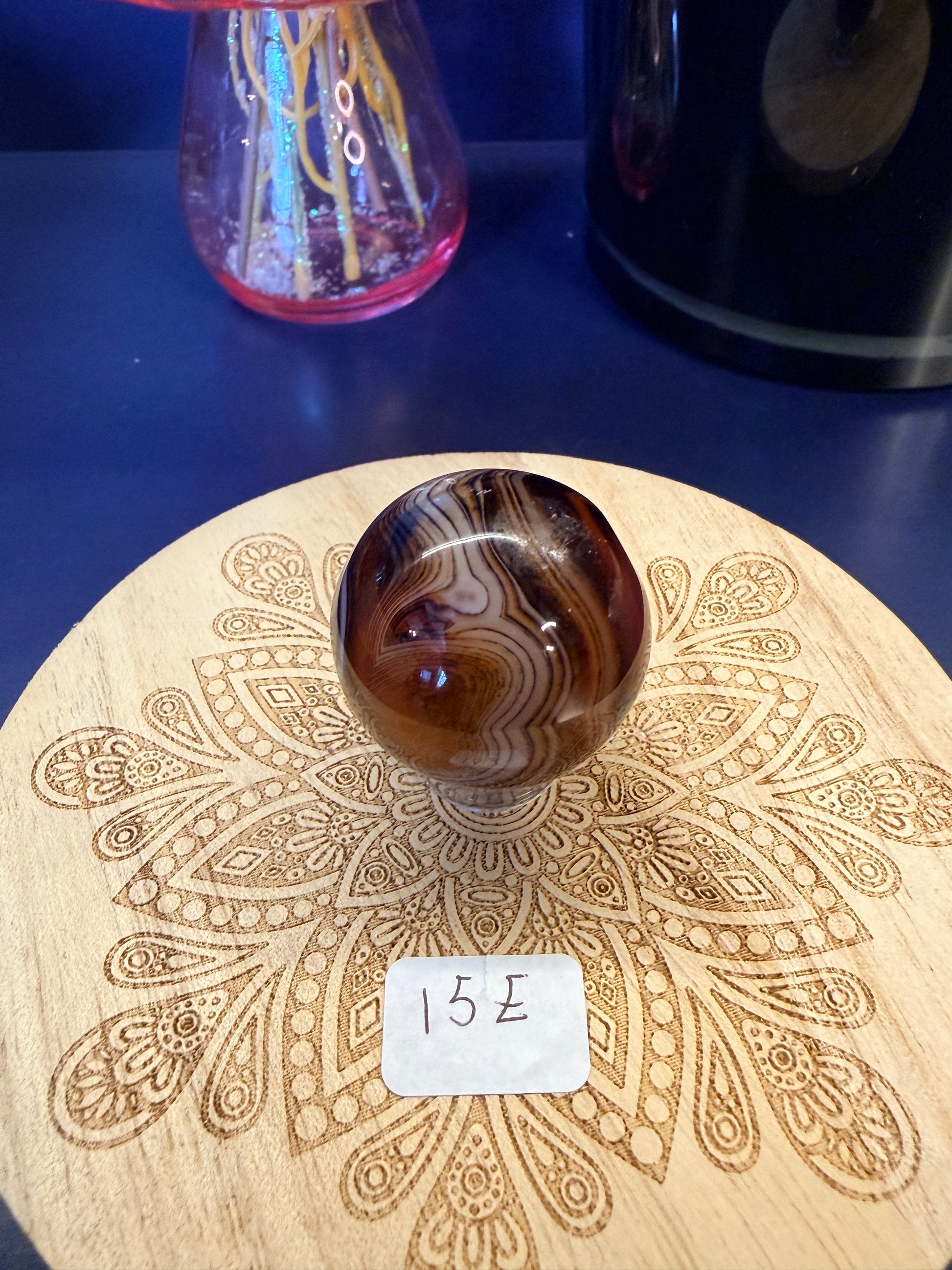 A red and black crystal sphere sitting on a decorative wooden coaster in front of a glass mushroom and black jar