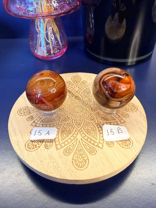 Two red and black crystal spheres sitting on a decorative wooden coaster in front of a glass mushroom and black jar