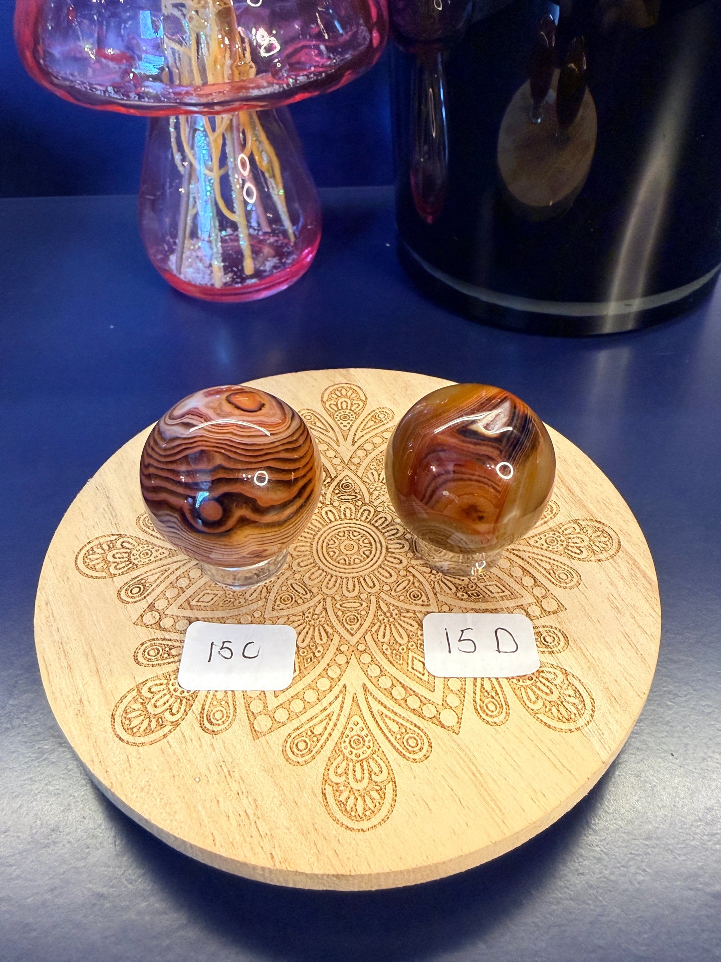 Two red and black crystal spheres sitting on a decorative wooden coaster in front of a glass mushroom and black jar