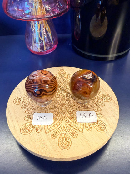 Two red and black crystal spheres sitting on a decorative wooden coaster in front of a glass mushroom and black jar