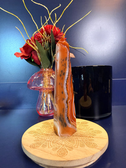 A black, white, and red sardonyx tower sitting on a decorative wooden coaster in front of a mushroom vase and black jar