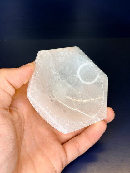Hand holding a white hexagonal selenite bowl on a blue background