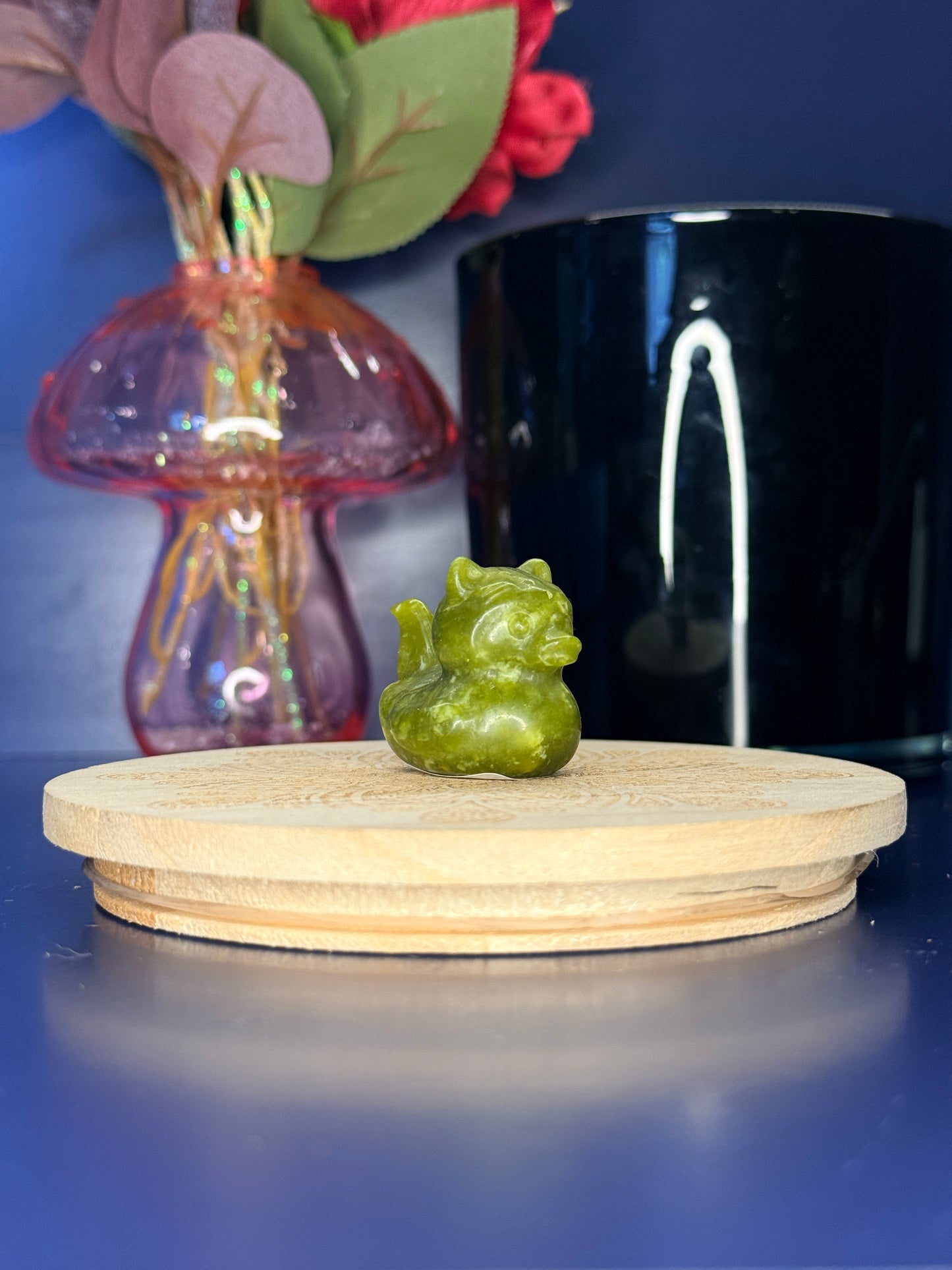 Serpentine kitty duck carving in front of a pink vase and black jar on a wooden coaster against a blue background