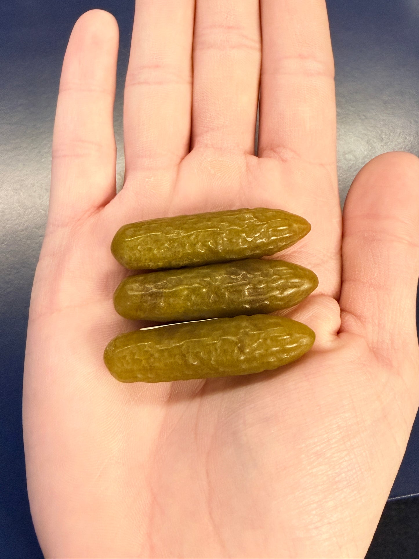 Three green crystal pickles sitting on an outstretched hand against a blue background