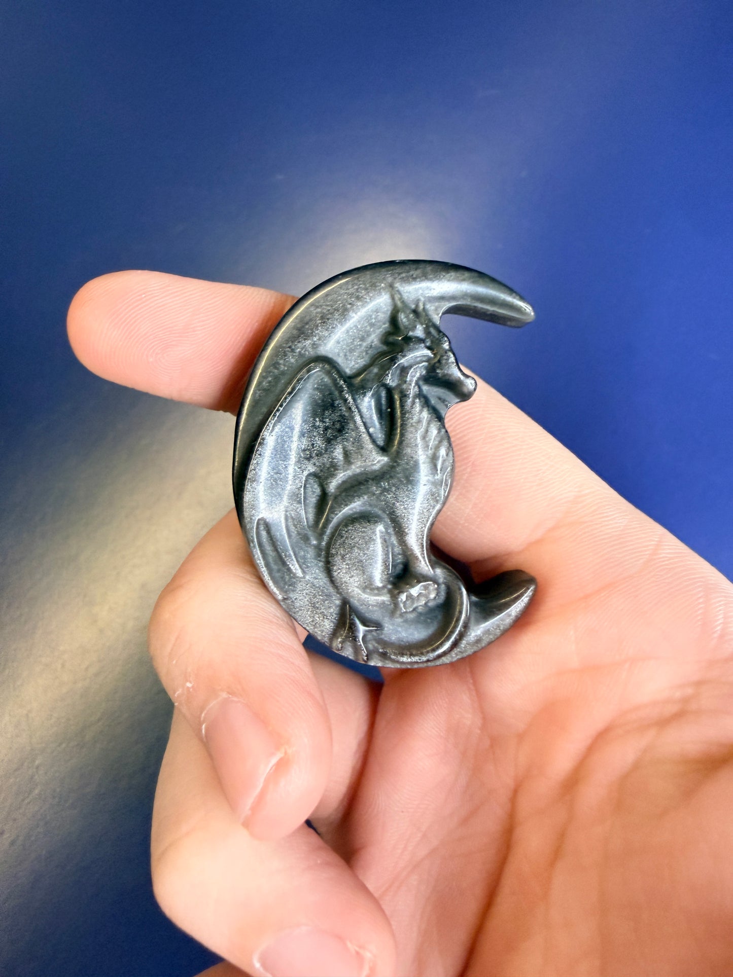 Hand holding a silver and black obsidian dragon in a moon against a blue background