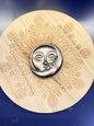 Silver and black obsidian sun & moon shape sitting on a decorative wooden coaster against a blue background