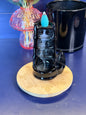 Black waterfall incense burner with a blue incense cone on top, in front of a pink mushroom and black jar on a blue background