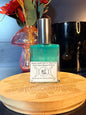 Perfume bottle with green liquid on a wooden surface with flowers and a black jar
