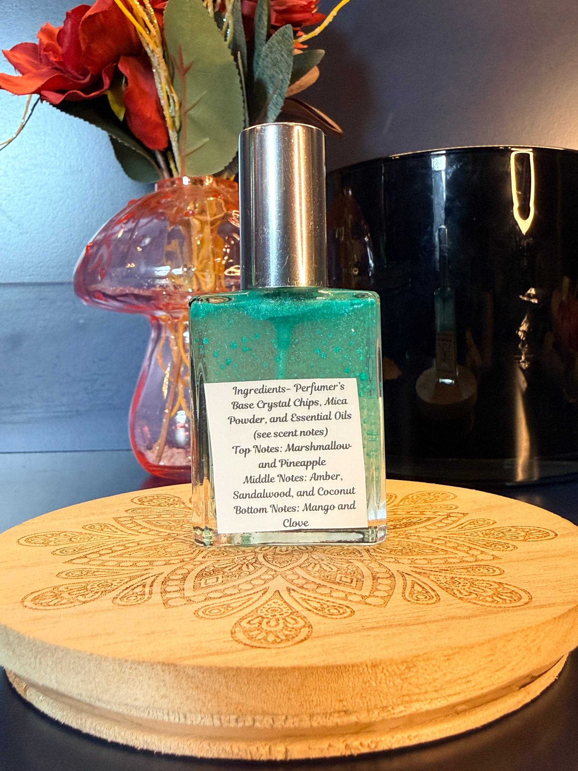 Perfume bottle with green liquid on a wooden surface with flowers and a black jar
