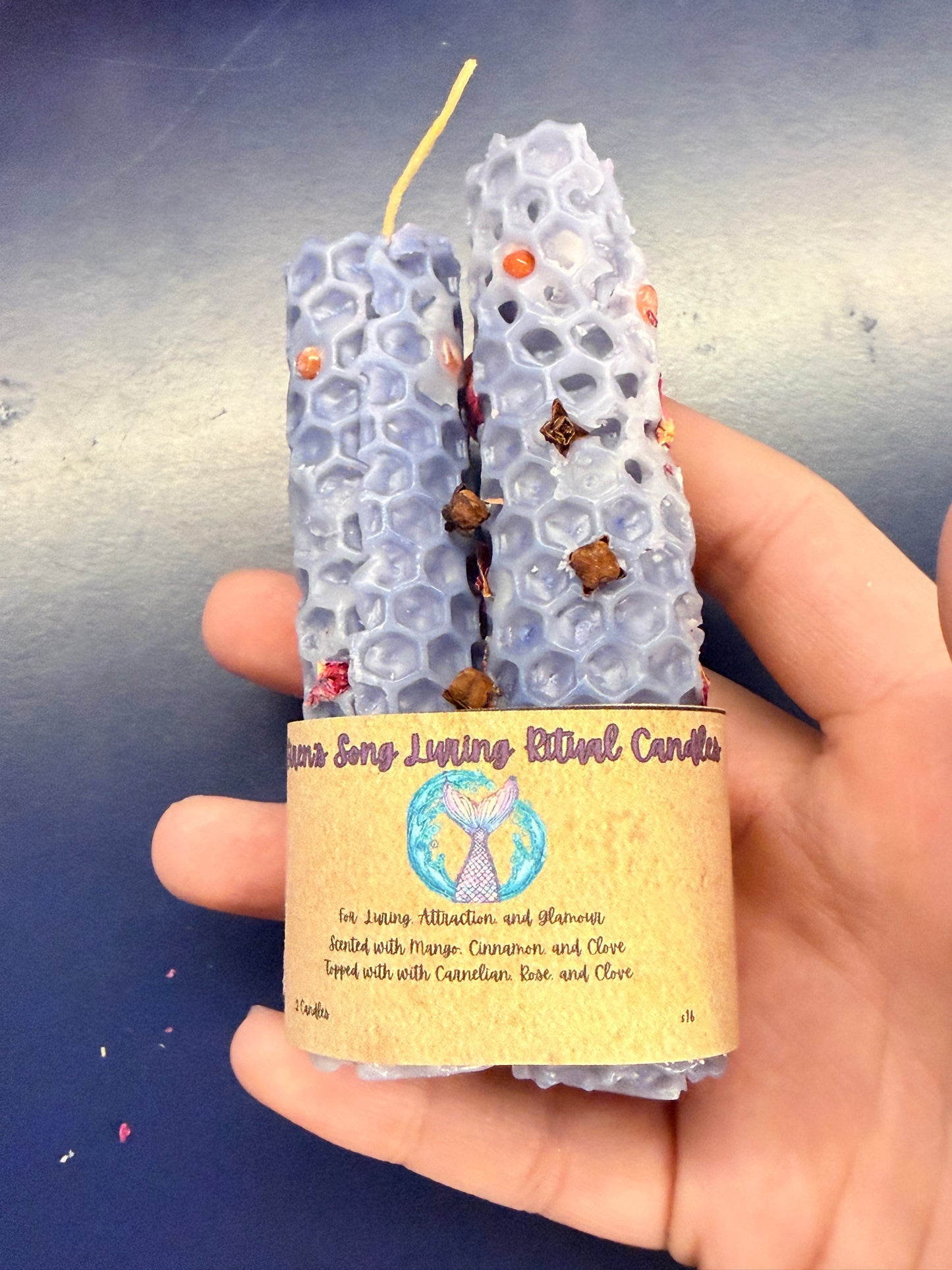Hand holding a two blue candles with a cardboard wrap on a blue surface