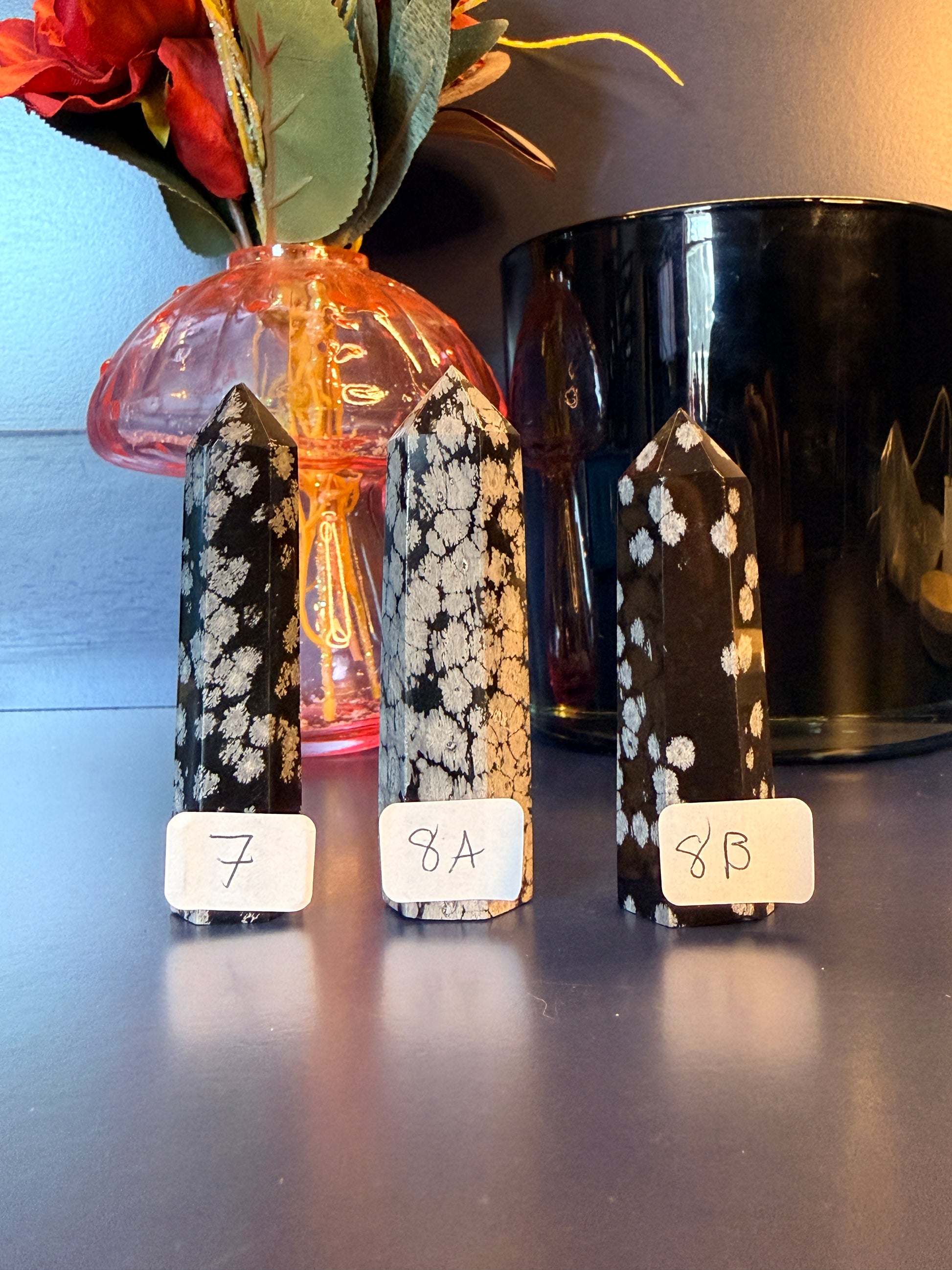 Three black and grey crystal towers sitting on a decorative wooden coaster in front of a glass mushroom and black jar