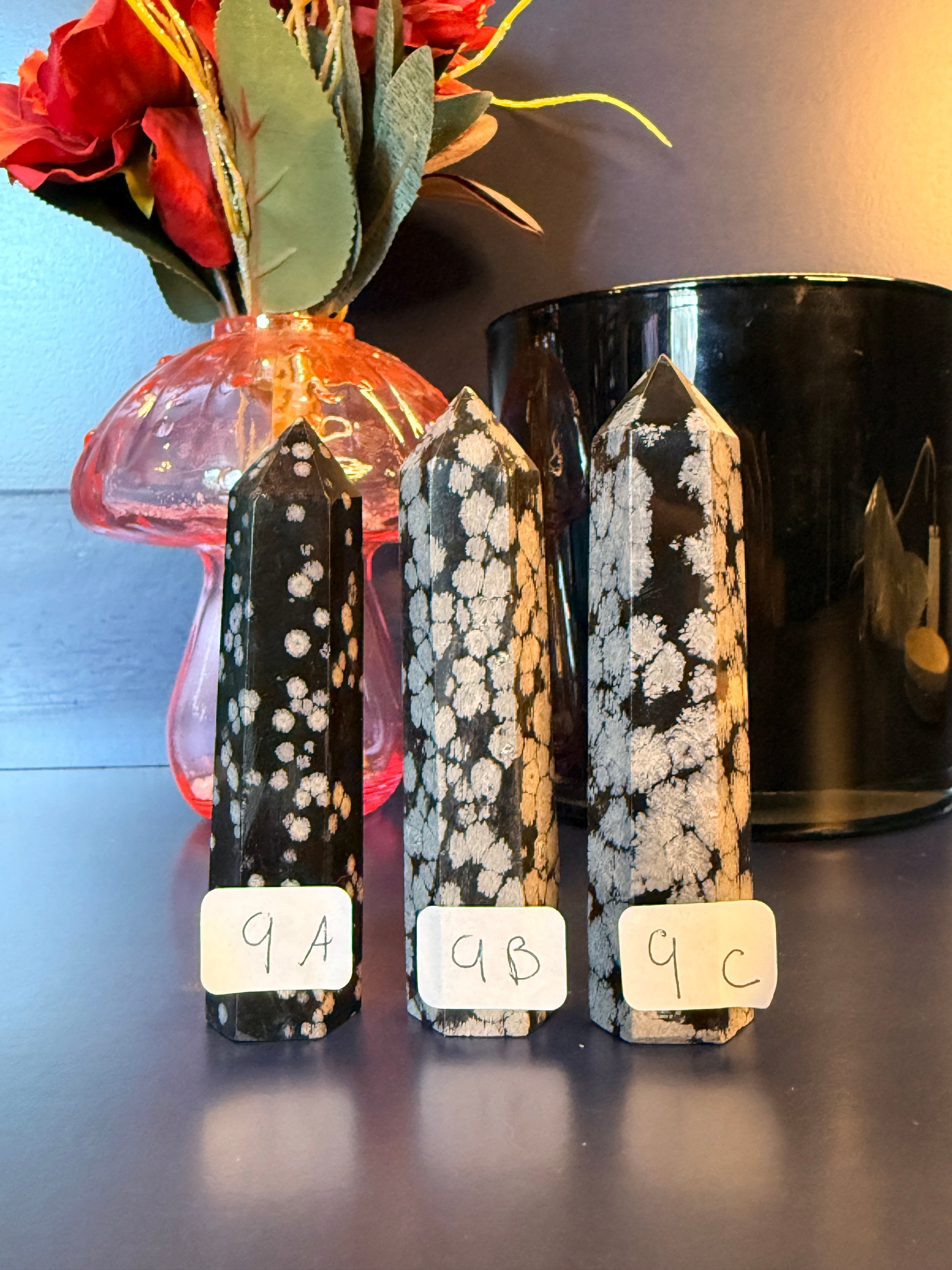 Three black and grey crystal towers sitting on a decorative wooden coaster in front of a glass mushroom and black jar