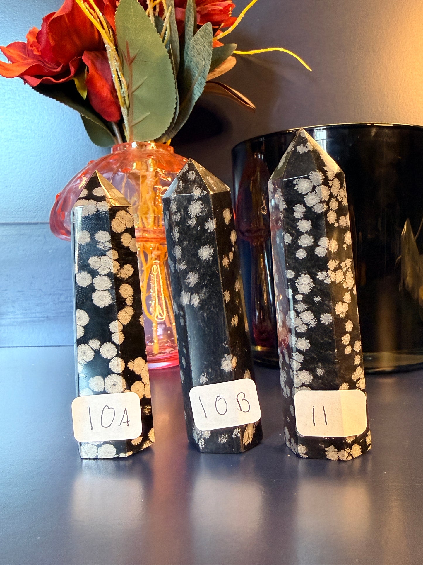 Three black and grey crystal towers sitting on a decorative wooden coaster in front of a glass mushroom and black jar