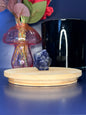 Blue and grey sodalite owl carving in front of a pink vase and black jar on a wooden coaster against a blue background