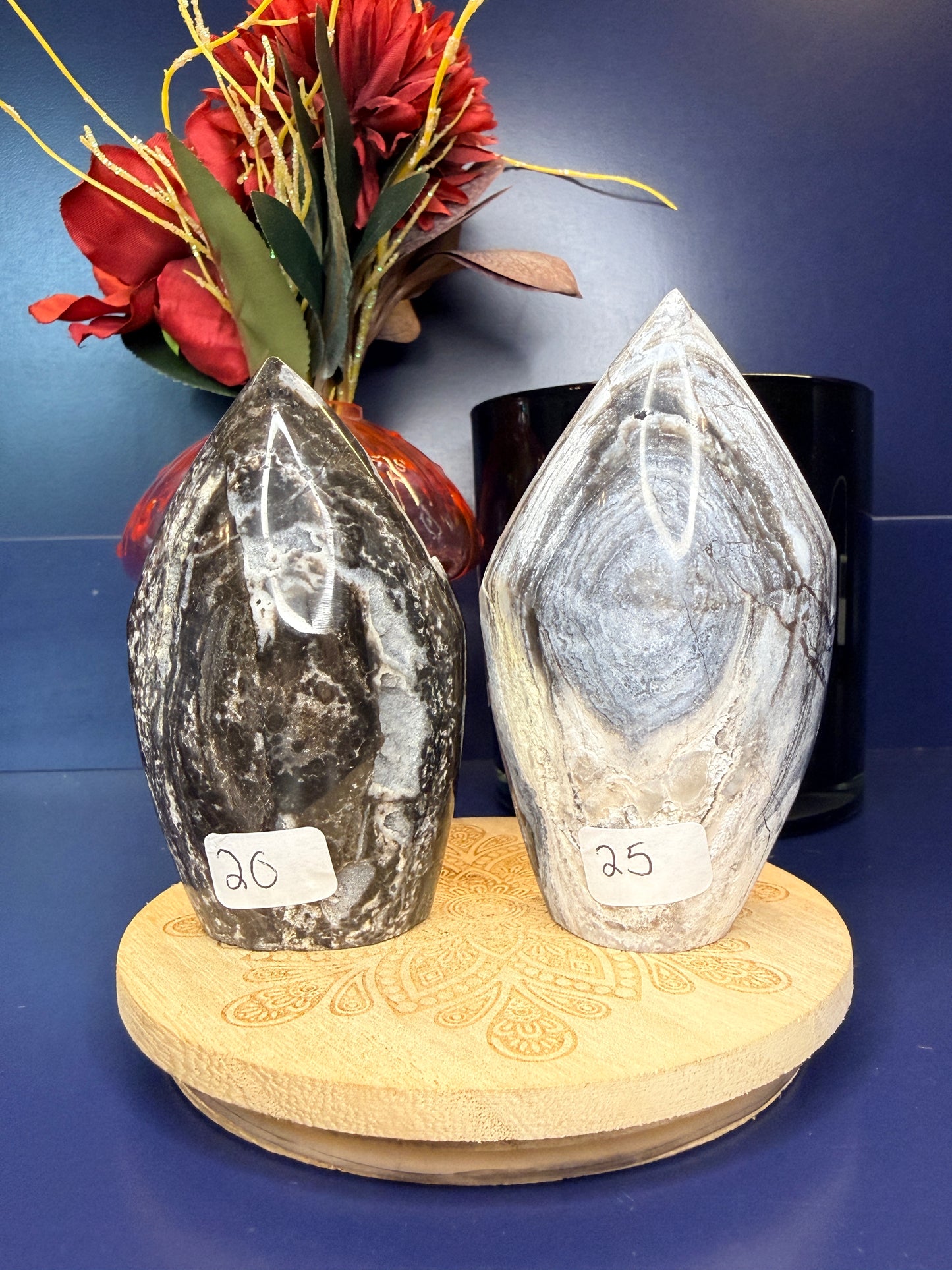 Two black and grey sphalerite freeforms on a wooden coaster in front of a red flower in a vase and black jar