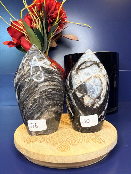 Two grey and white sphalerite freeforms on a wooden coaster in front of a red flower in a vase and black jar