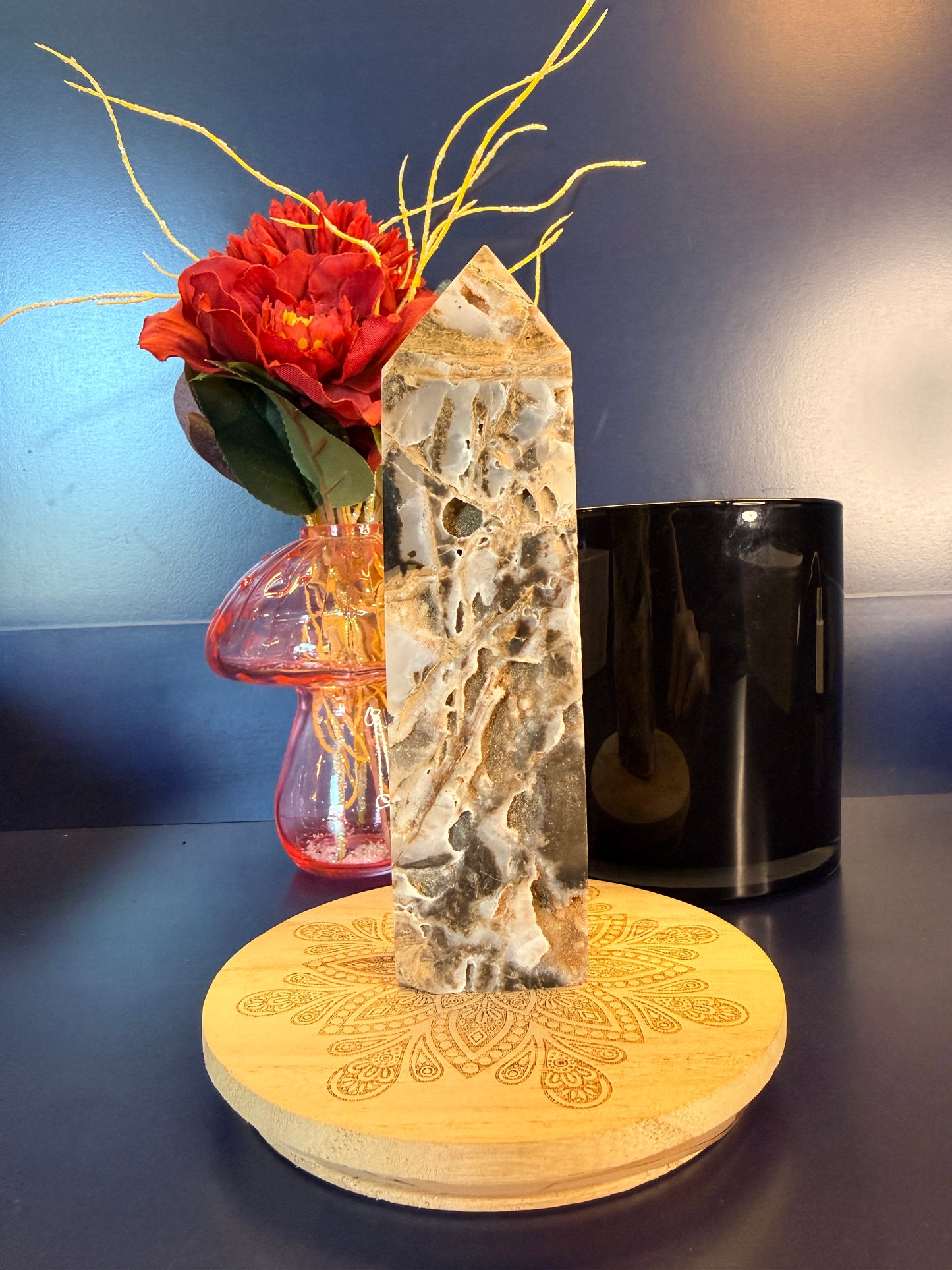 Large crystal tower with an intricate pattern on a decorative wooden coaster in front of a red flower and black jar