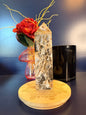 Large crystal tower with an intricate pattern on a decorative wooden coaster in front of a red flower and black jar