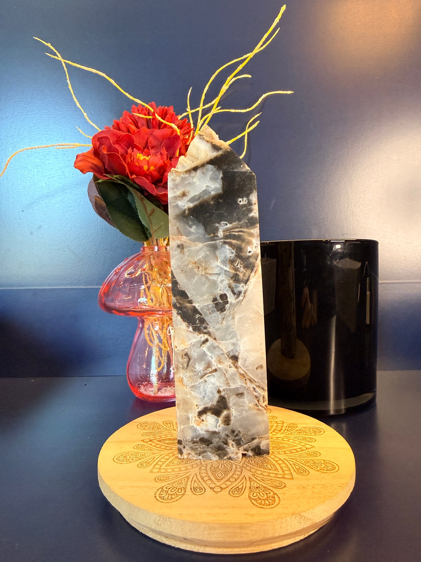 Large crystal tower with an intricate pattern on a decorative wooden coaster in front of a red flower and black jar