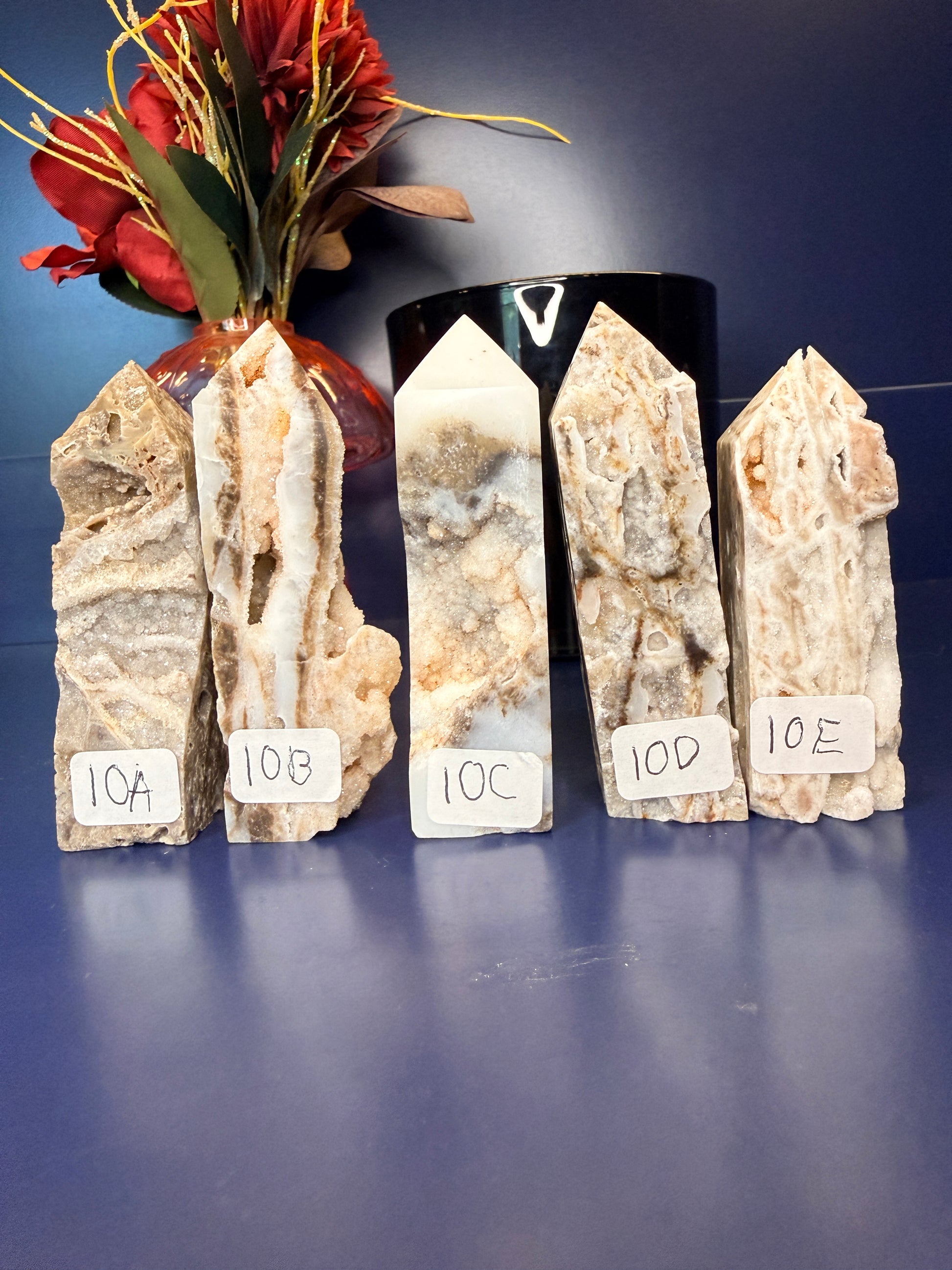 Five intricate sphalerite towers in front of a red flower in a vase and black jar on a blue background