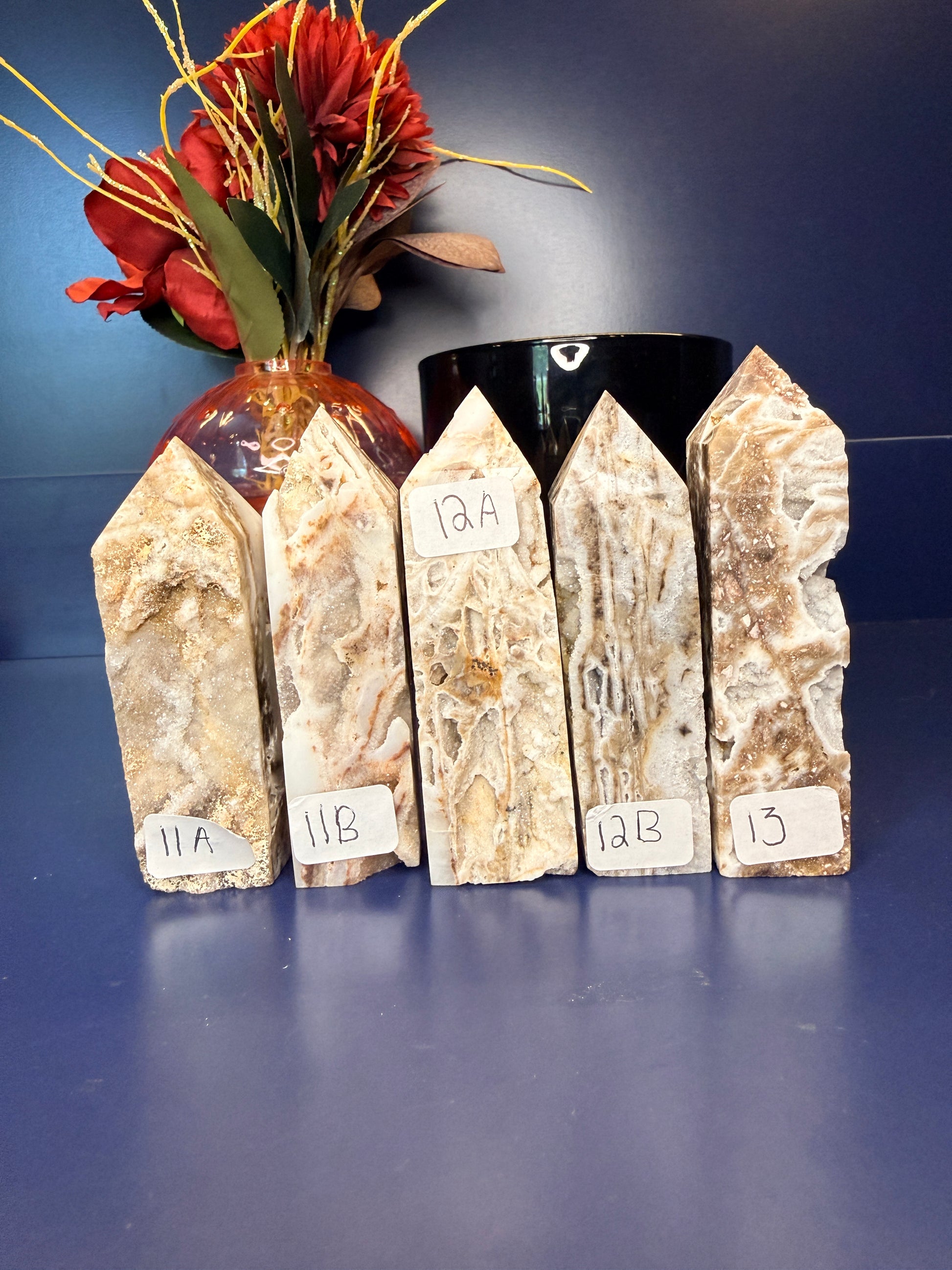 Five intricate sphalerite towers in front of a red flower in a vase and black jar on a blue background