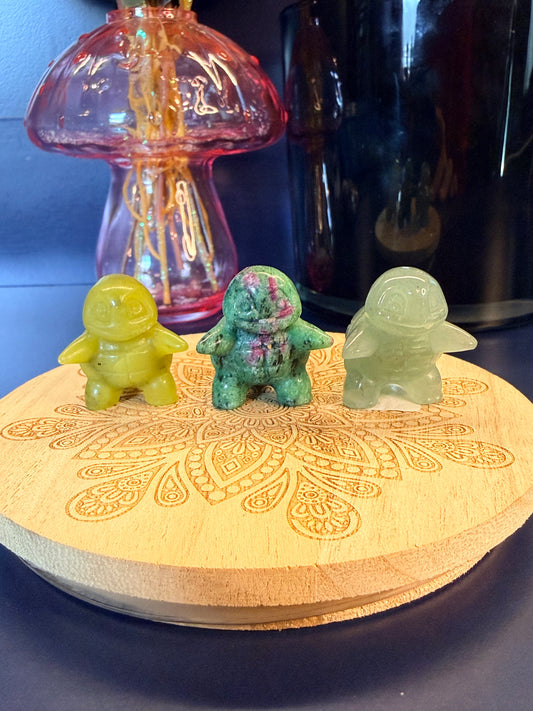Three different squirtle crystals sitting on a decorative wooden coaster in front of a glass mushroom and black jar