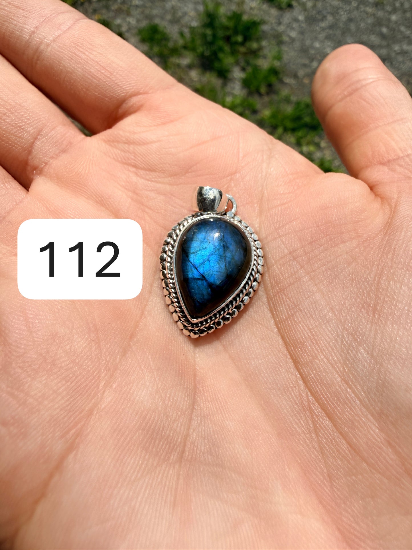 Hand holding a labradorite pendant set in sterling silver against a blurred nature background