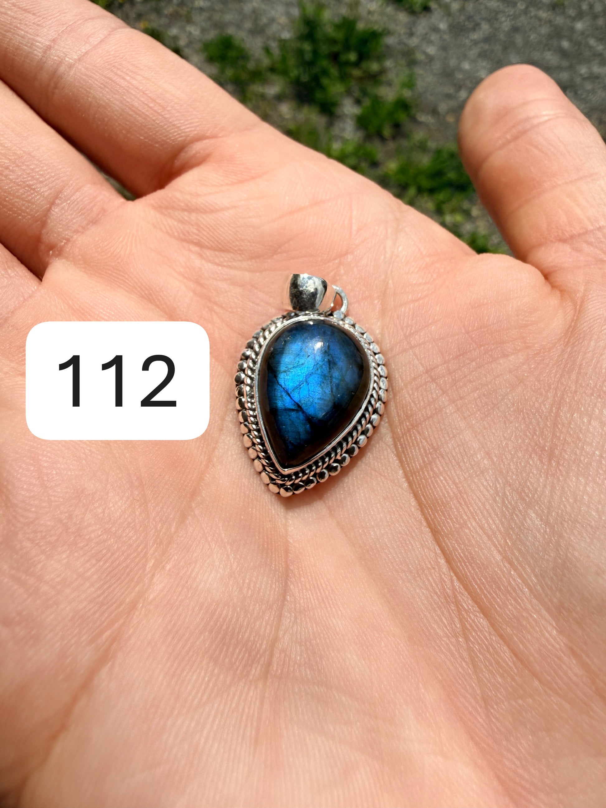 Hand holding a labradorite pendant set in sterling silver against a blurred nature background