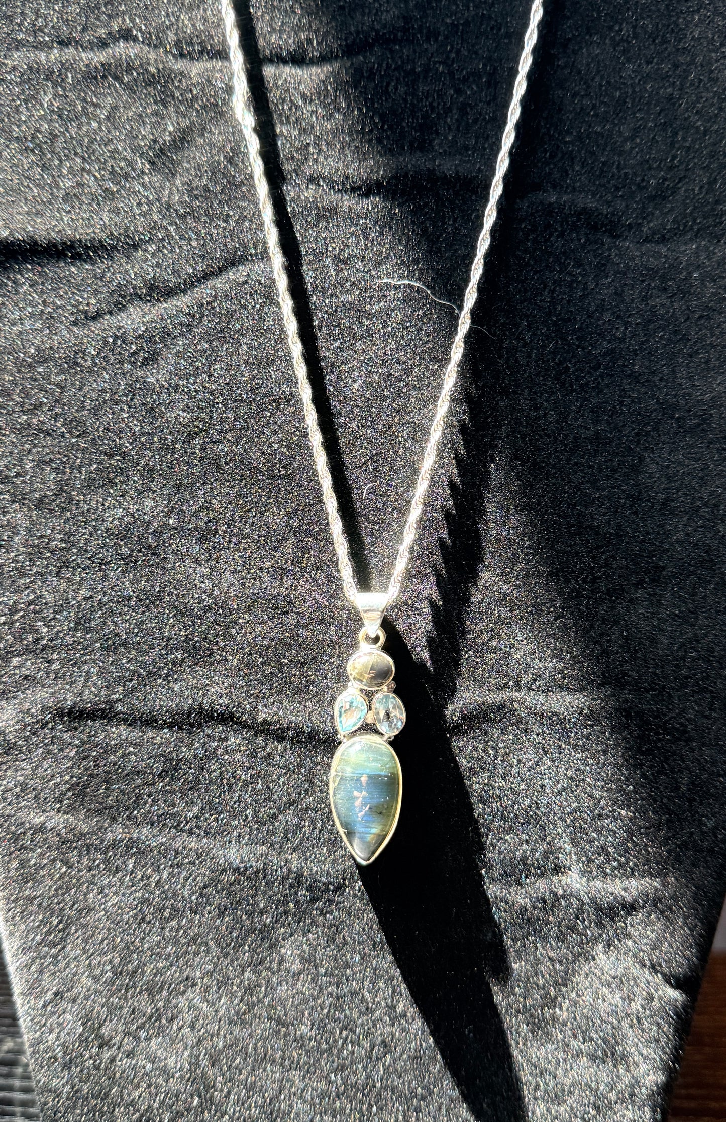 Sterling silver necklace resting on a black velvet jewelry stand holding an ovular labradorite pendant