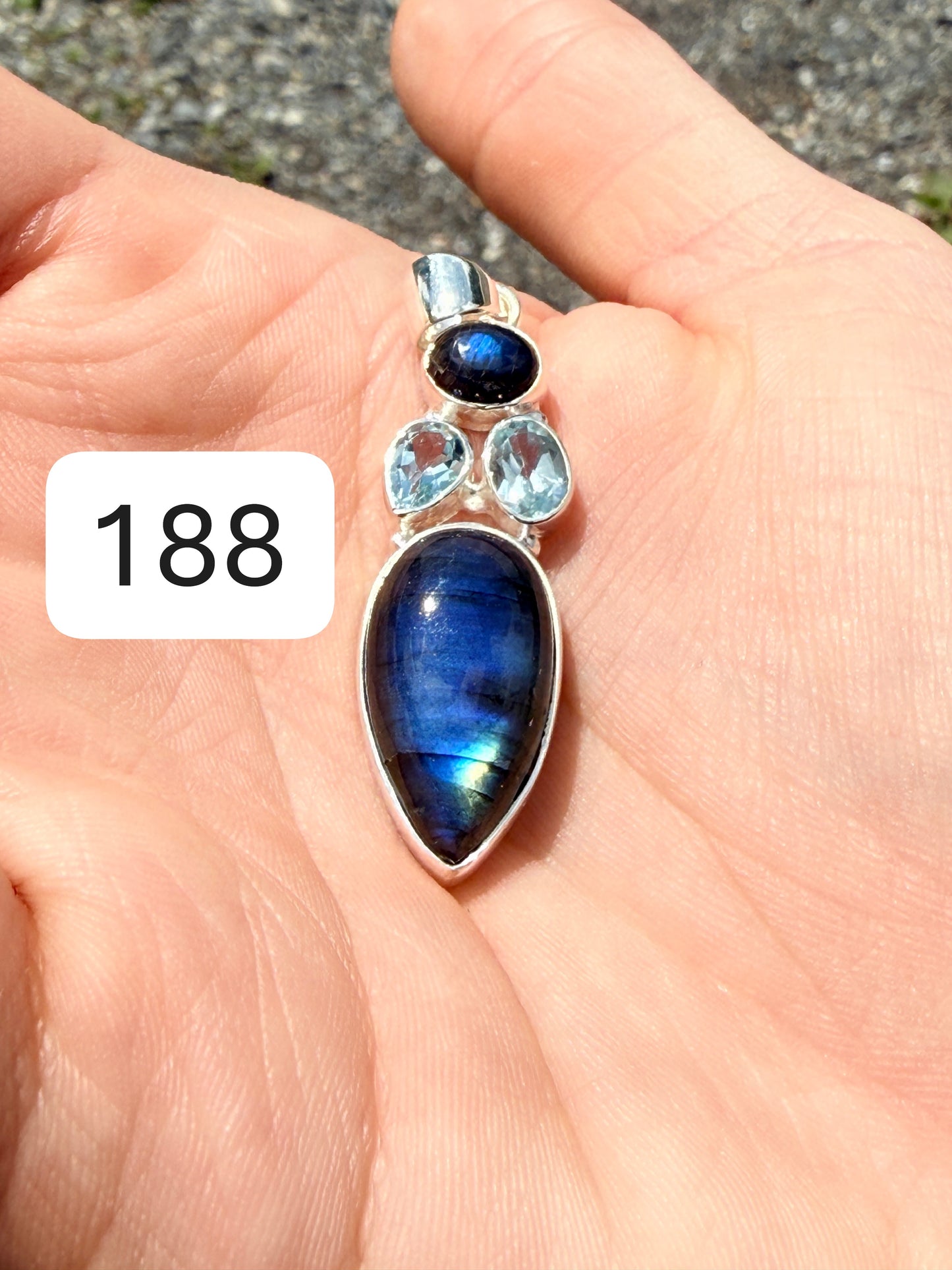 Hand holding a flashing labradorite pendant with two aquamarines set above it in sterling silver