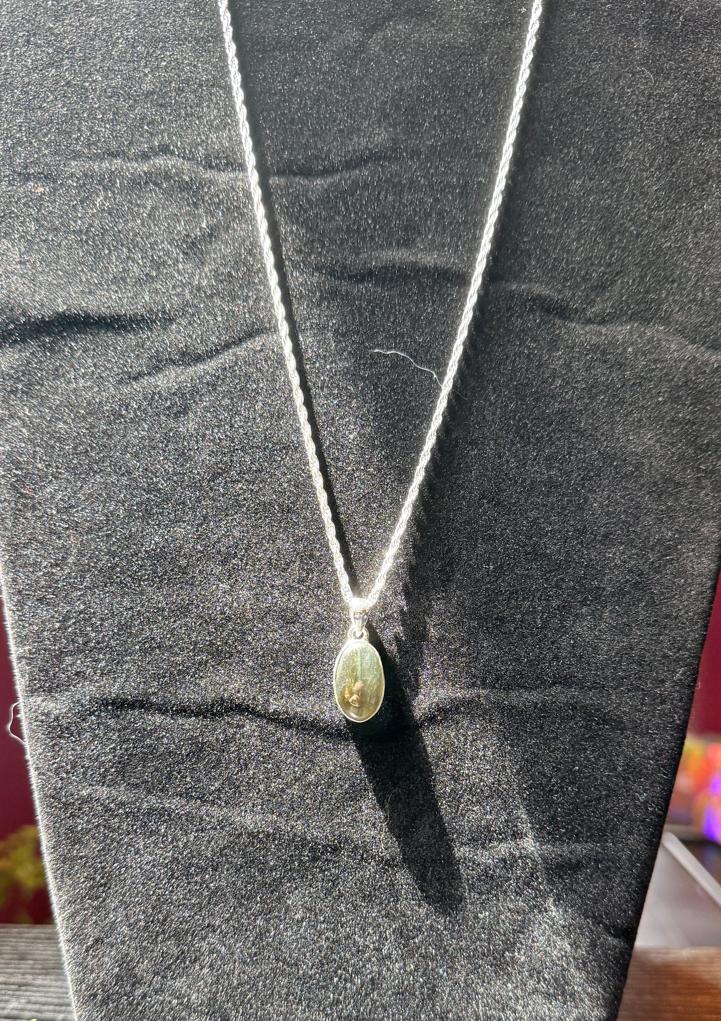 Sterling silver necklace resting on a black velvet jewelry stand holding an ovular labradorite pendant