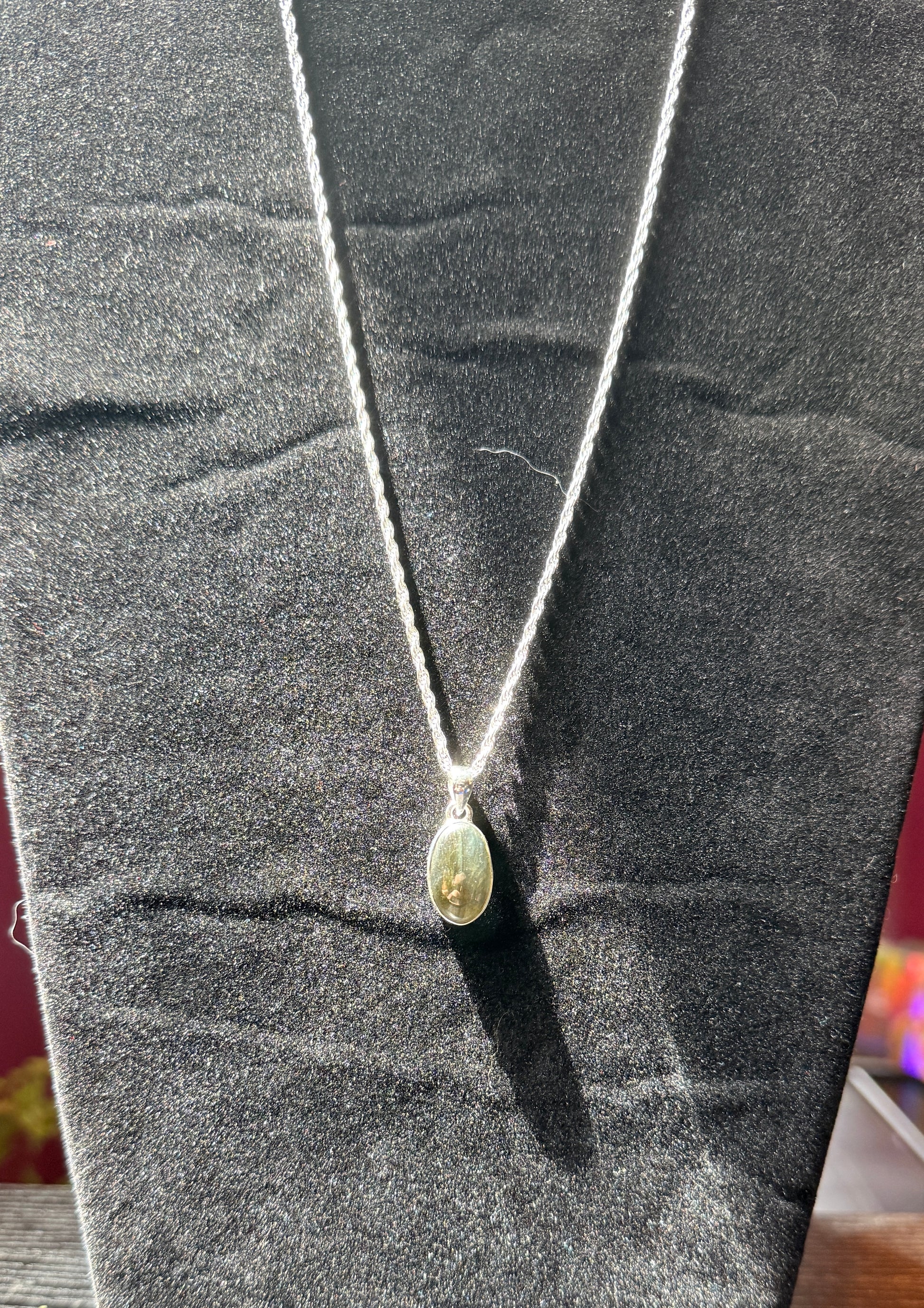 Sterling silver necklace resting on a black velvet jewelry stand holding an ovular labradorite pendant