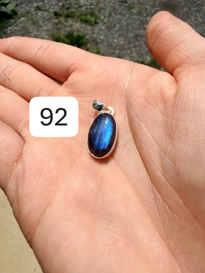 Hand holding an ovular labradorite pendant set in sterling silver against a blurred nature background