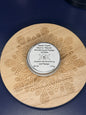 Circular labeled lip balm container on a decorative wooden coaster on a blue background