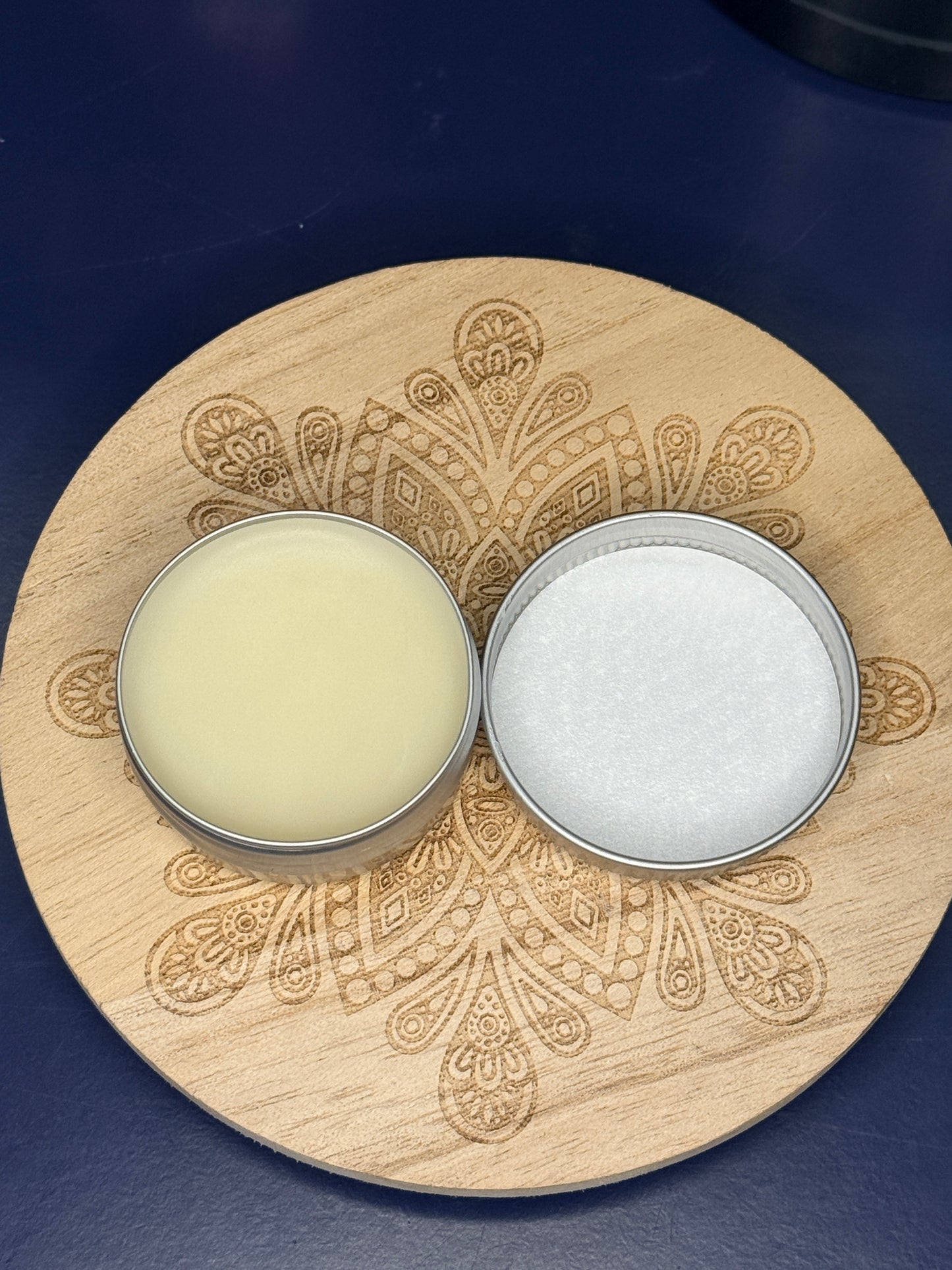 Open circular lip balm container on a decorative wooden coaster on a blue background