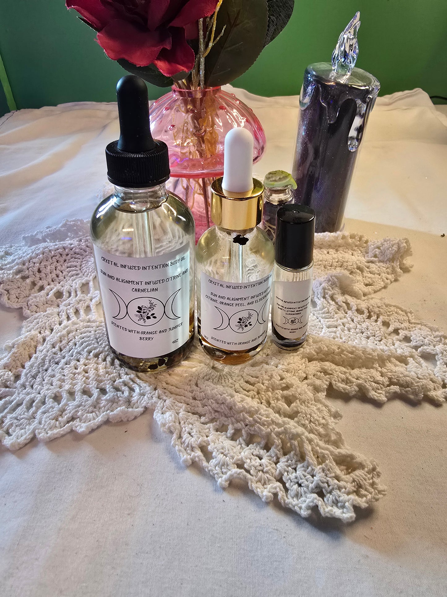 Three glass bottles filled with clear body oil with herbs on a white crochet mat and white table cloth