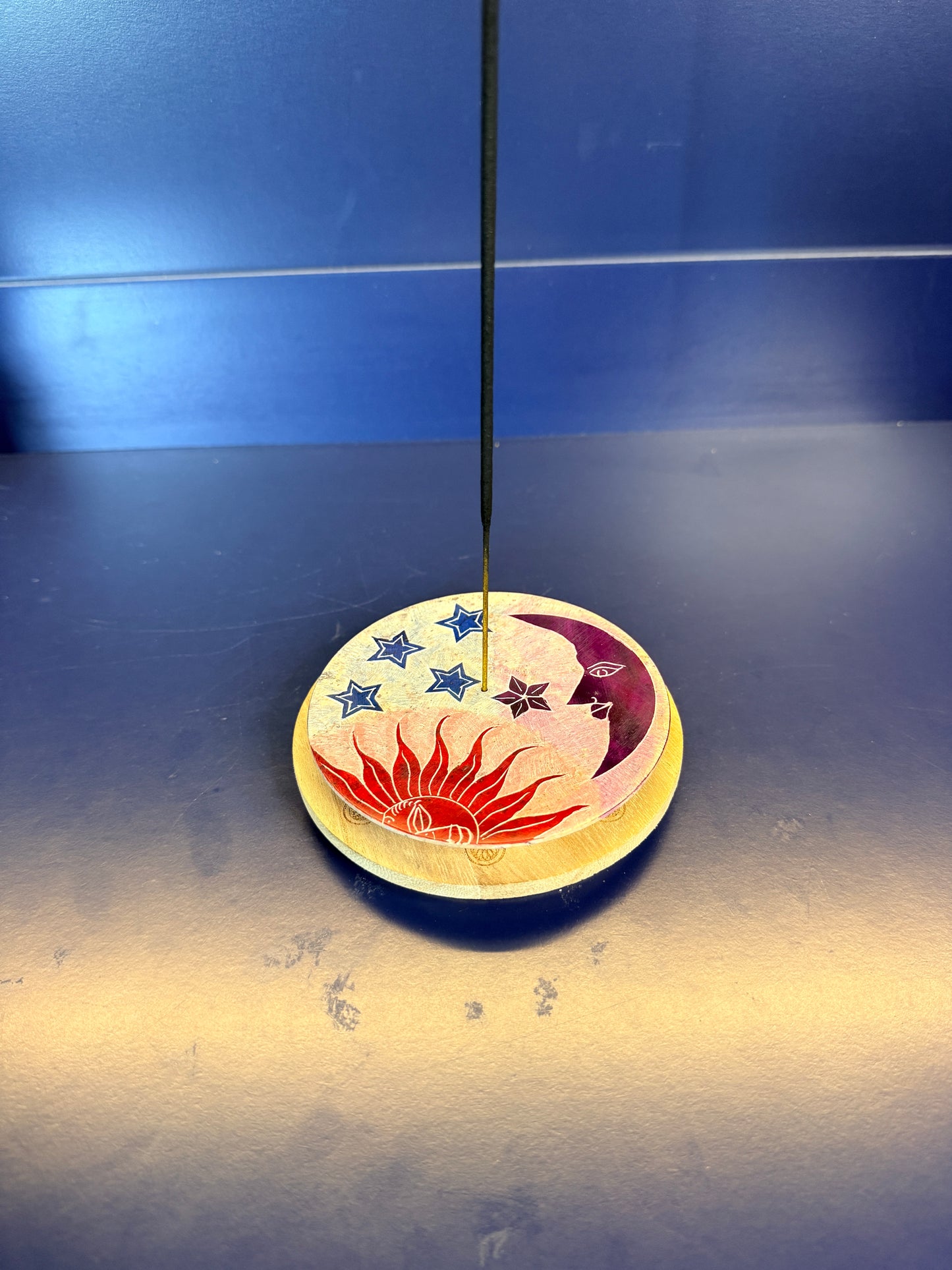 Round incense burner with a sun, star, and moon design holding an incense stick on a blue background