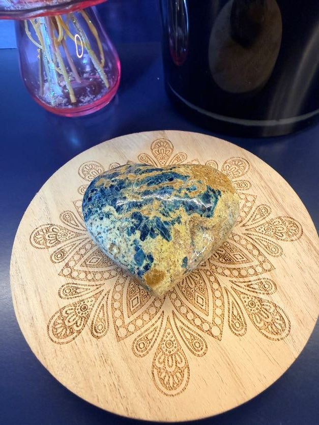 Speckled patterned blue and light red heart sitting on a decorative wooden coaster on a blue background