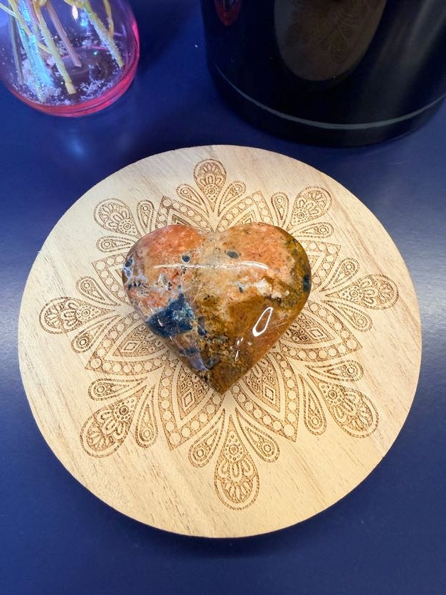 Speckled patterned red and blue heart sitting on a decorative wooden coaster on a blue background