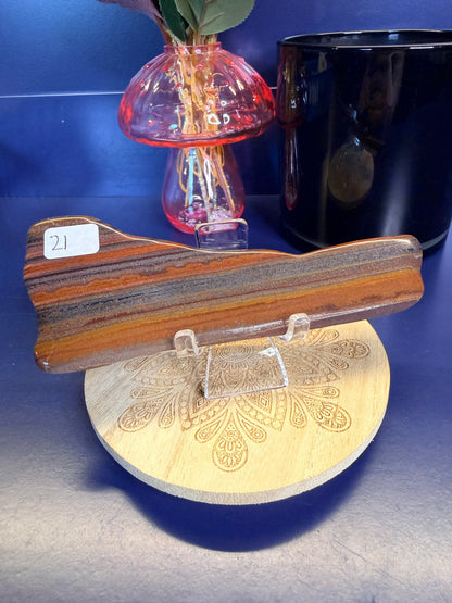 Long brown and steel grey tiger iron slab on a decorative wooden slab in front of a mushroom and black jar