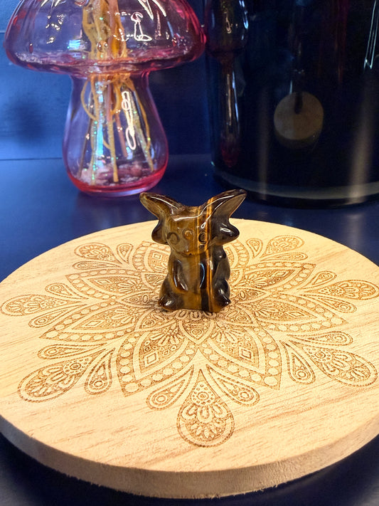 A tiger's eye espeon crystal sitting on a decorative wooden coaster in front of a glass mushroom and black jar